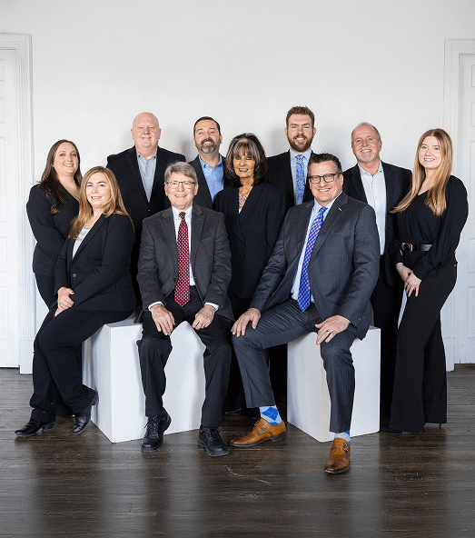 A group of ten people in business attire pose against a white wall. They appear professional and confident, with neutral expressions.
